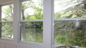 A room with three windows overlooking a lake, surrounded by trees. - Avon Lakeshore - Waterfront retreat with hot tub! (Maryland)