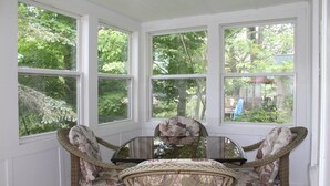 A room with a glass table surrounded by wicker chairs, large windows with a view of trees. - Avon Lakeshore - Waterfront retreat with hot tub! (Maryland)