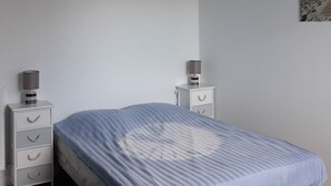 A bedroom with a bed, two bedside tables, a lamp, and a painting on the wall. - Apartment with panoramic sea view over the bay of Perros Guirec (Perros Guirec)