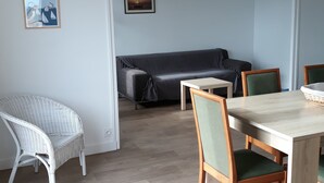 A room with a dining table, chairs, a sofa, and two framed pictures on the wall. - Apartment with panoramic sea view over the bay of Perros Guirec (Perros Guirec)
