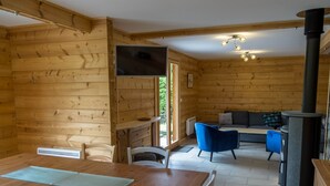 A wooden cabin interior with a dining table, chairs, a sofa, and a fireplace. - Chalet 6 people, Gérardmer, Les Bas-Rupts (Gérardmer)