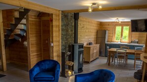 A cozy cabin interior with a wooden staircase, a stone fireplace, a kitchen area, and two blue armchairs. - Chalet 6 people, Gérardmer, Les Bas-Rupts (Gérardmer)