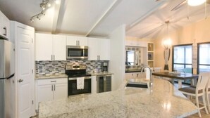 A modern kitchen with white cabinets, a granite countertop, stainless steel appliances, and a dining area with a table and chairs. - Short walk to the beach * Montego Bay;Ocean City, MD (Ocean City)