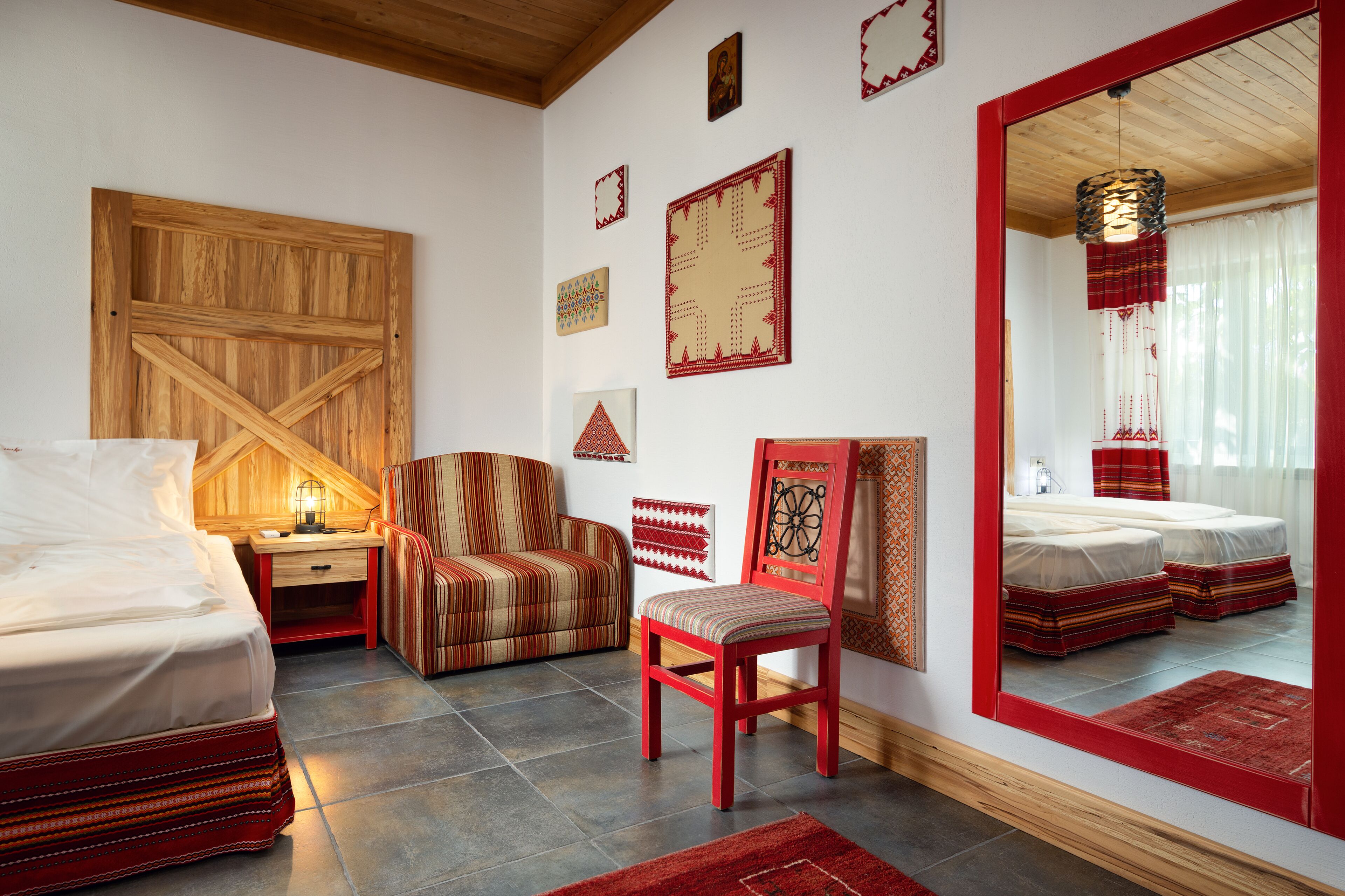 A bedroom with a bed, a chair, a nightstand, a mirror, and decorative wall art.