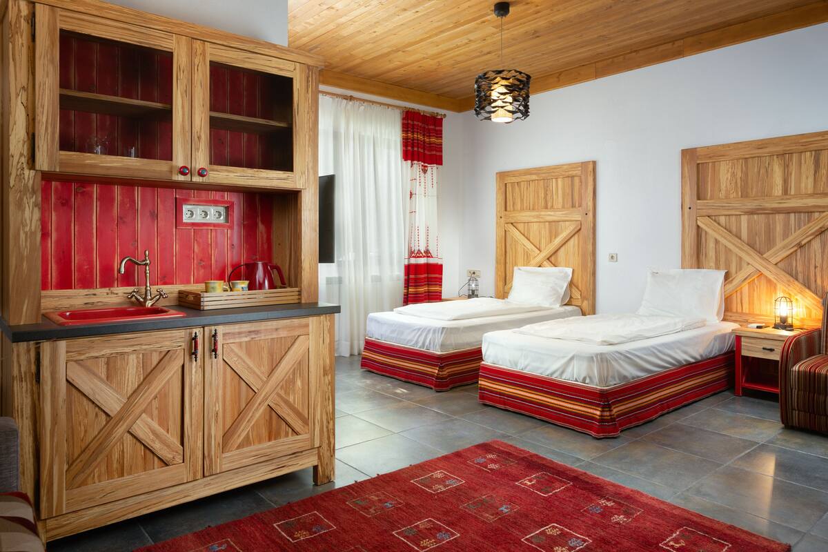 A room with two beds, a wooden cabinet with a sink, and a red rug.
