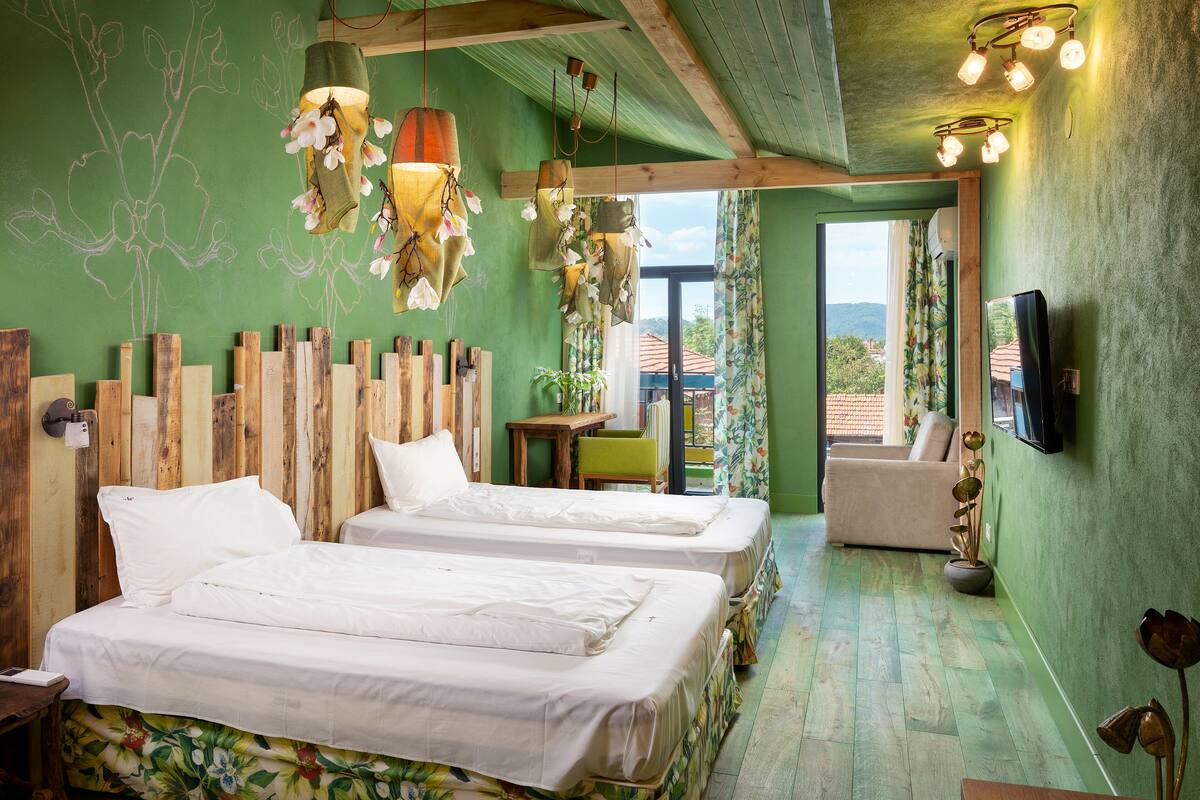 A room with two beds, wooden headboards, hanging floral lights, a TV, and a view of the outdoors.