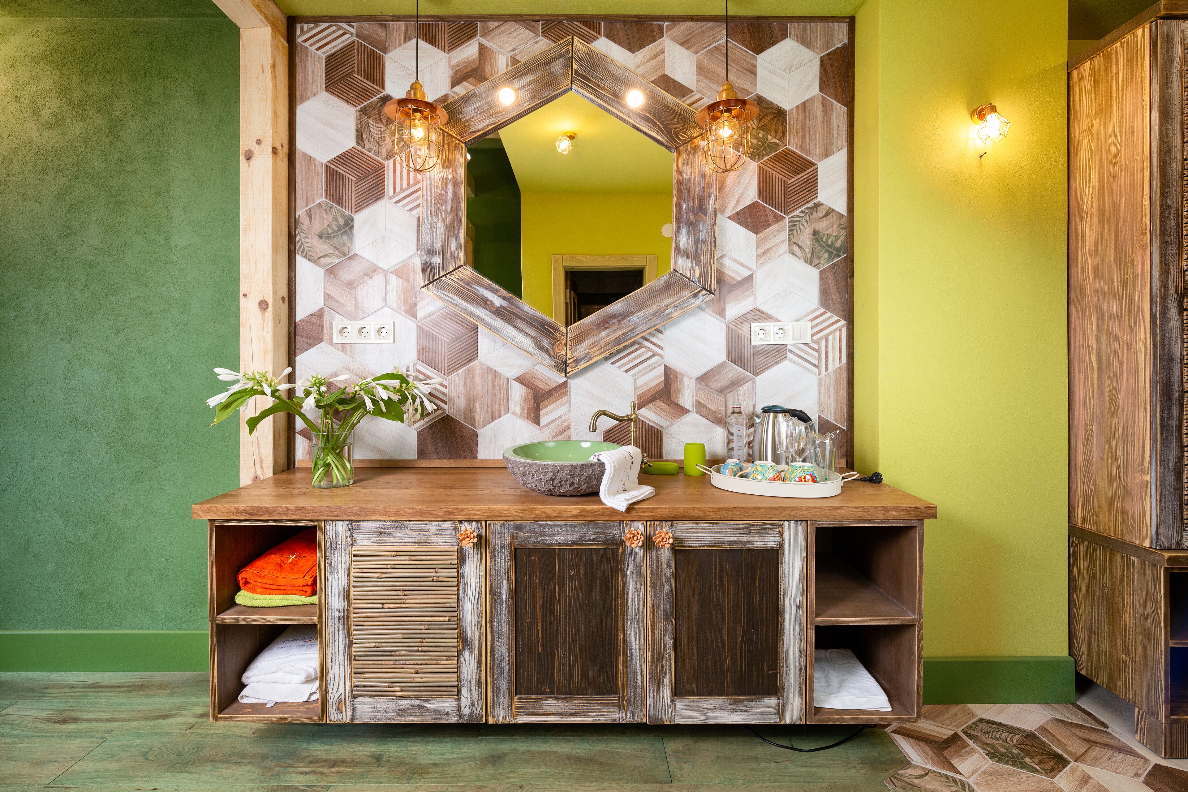 Une salle de bain avec un meuble-lavabo en bois, un mur vert et un miroir agrémenté d’un pare-splash en carreaux géométriques.