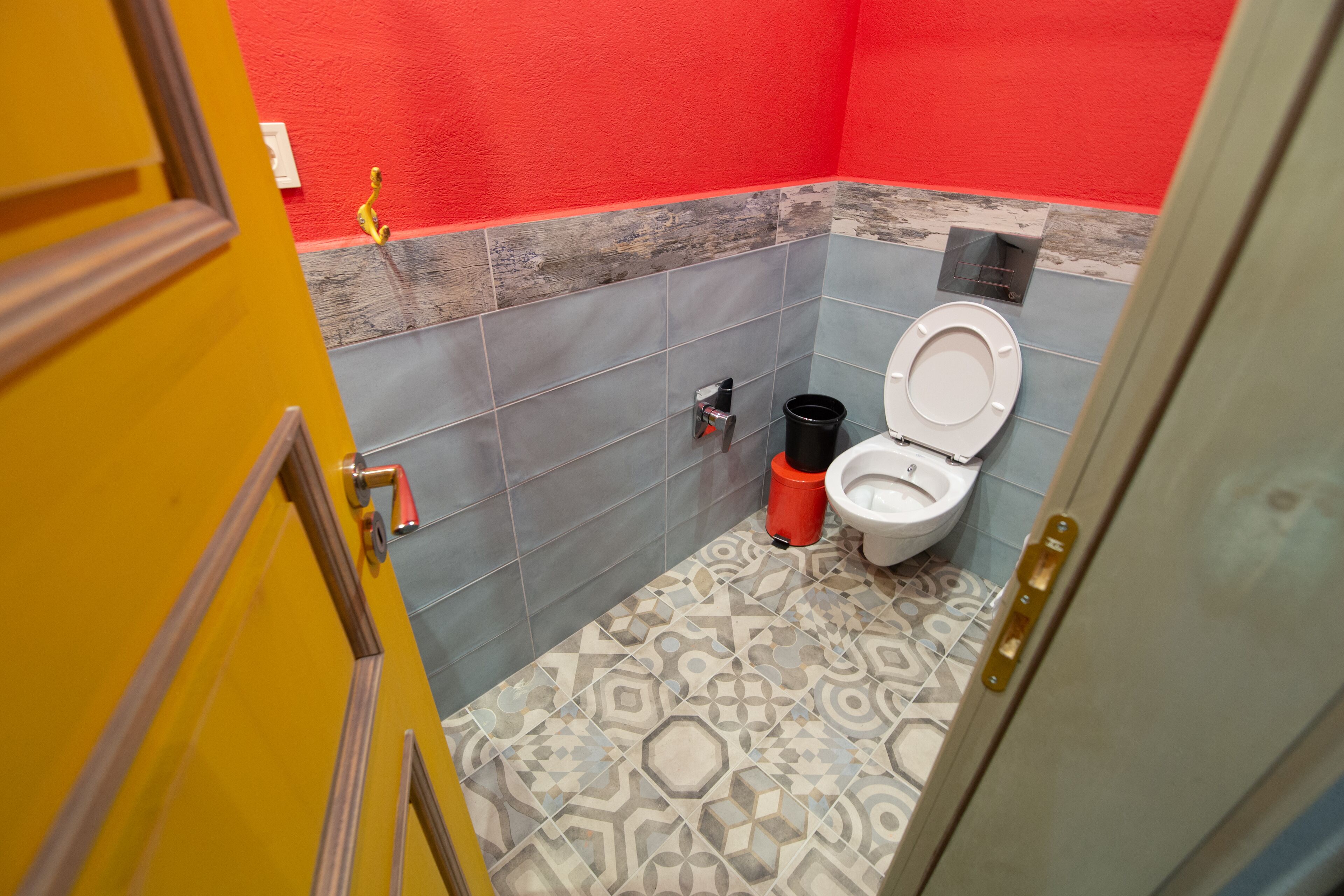 A bathroom with a toilet, a trash bin, and a red wall.