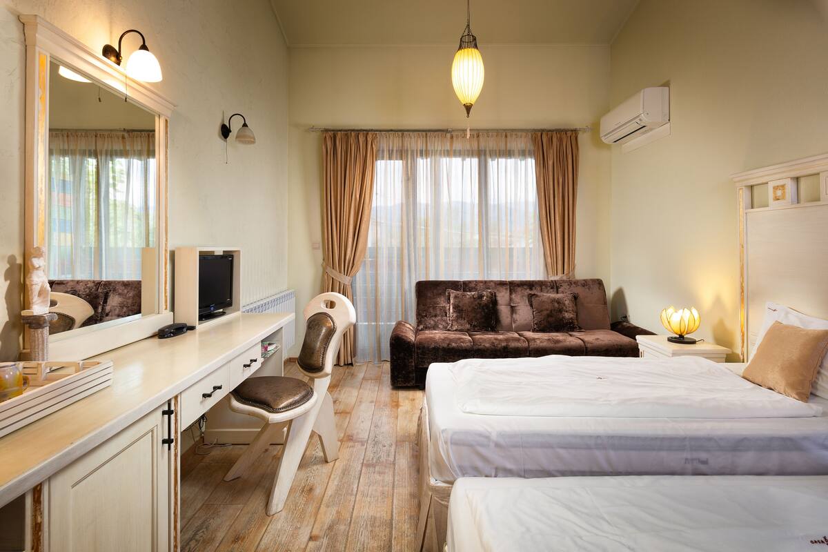 A hotel room with a bed, a desk, a chair, a sofa, and a large mirror.