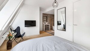 A modern bedroom with a large bed, a TV mounted on the wall, a wooden ladder, and a bathroom visible through an open door. - Luxurious rooftop penthouse with rooftop terrace, a balcony, bath, duo shower (Groningen)