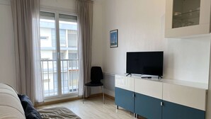 Una sala de estar moderna con un sofá, un televisor en un mueble bajo, una silla y un ventanal con cortinas.
