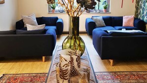 Un salon moderne avec deux canapés bleu foncé, un vase en verre orné de branches décoratives et des verres à motifs posés sur une table basse en bois.