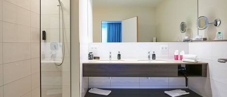 Un baño moderno con ducha de vidrio, lavamanos dobles y un espejo grande.