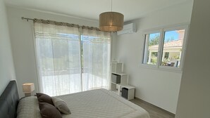 Une chambre avec un grand lit, une table de chevet avec une lampe, un luminaire au plafond et une vue sur l’extérieur par une fenêtre.