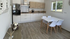 Une cuisine moderne avec des meubles blancs, une table à manger entourée de chaises blanches et une fenêtre donnant sur un paysage verdoyant.