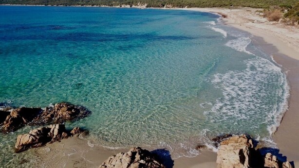 Un paysage côtier caractérisé par une eau turquoise et limpide, une côte rocheuse et des montagnes qui se dessinent à l’horizon.