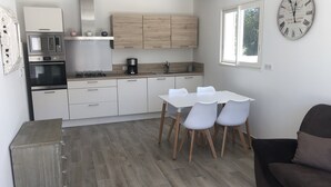 Une cuisine moderne avec des meubles blancs, un four encastré et une machine à café. On y trouve une table à manger avec quatre chaises et une horloge au mur.