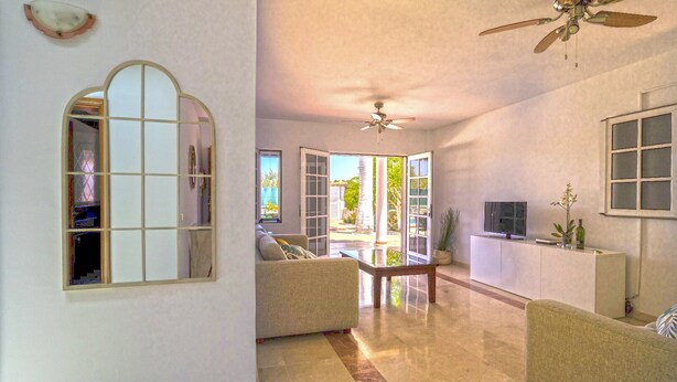 Un salón comedor amplio con ventilador de techo, un ventanal grande y un televisor sobre un mueble.
