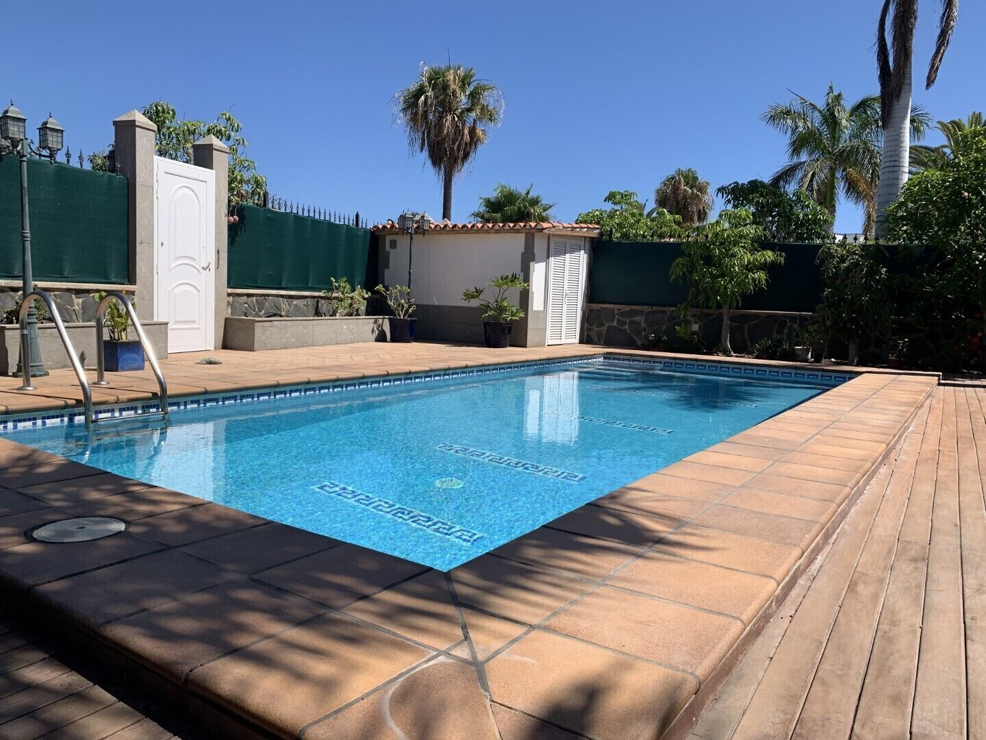 A rectangular swimming pool with a tiled deck surrounding it.