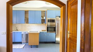 Una cocina con gabinetes azules, encimera de madera y electrodomésticos de acero inoxidable, incluyendo un microondas y un horno.