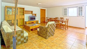 Una sala de estar con sofá, televisión, armarios de madera y una zona de comedor con sillas y mesa.