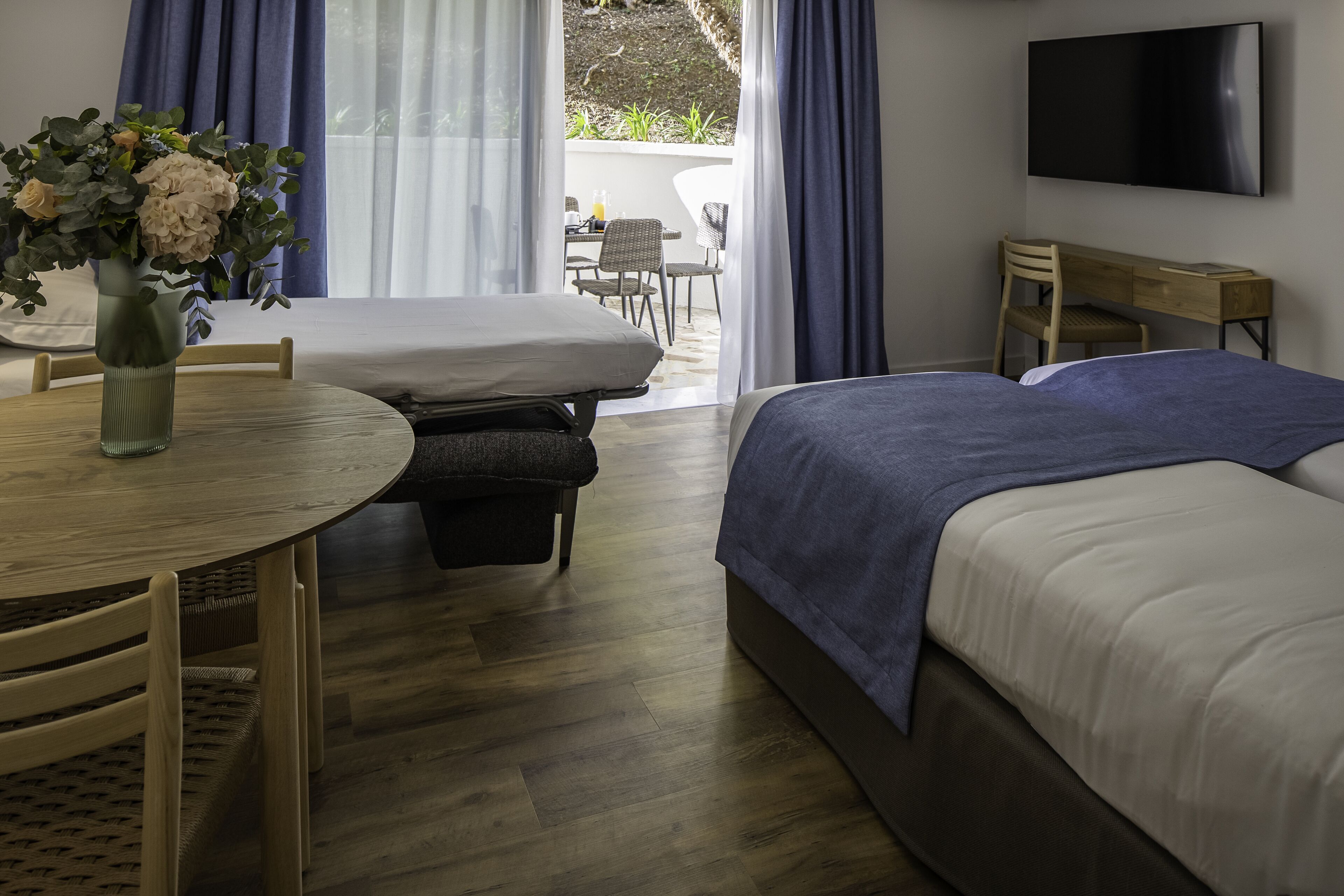 A hotel room with a bed, a desk, a chair, a table, and a TV.