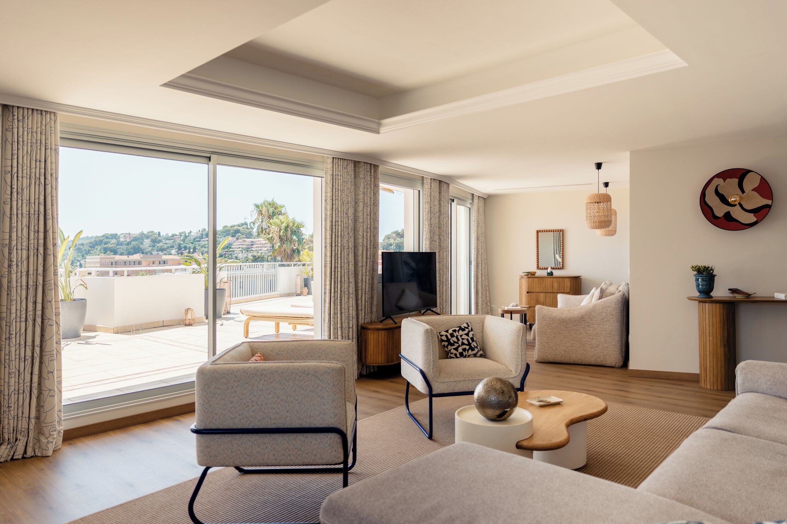 A modern living room with a large window, a flat-screen TV, and a cozy seating area.