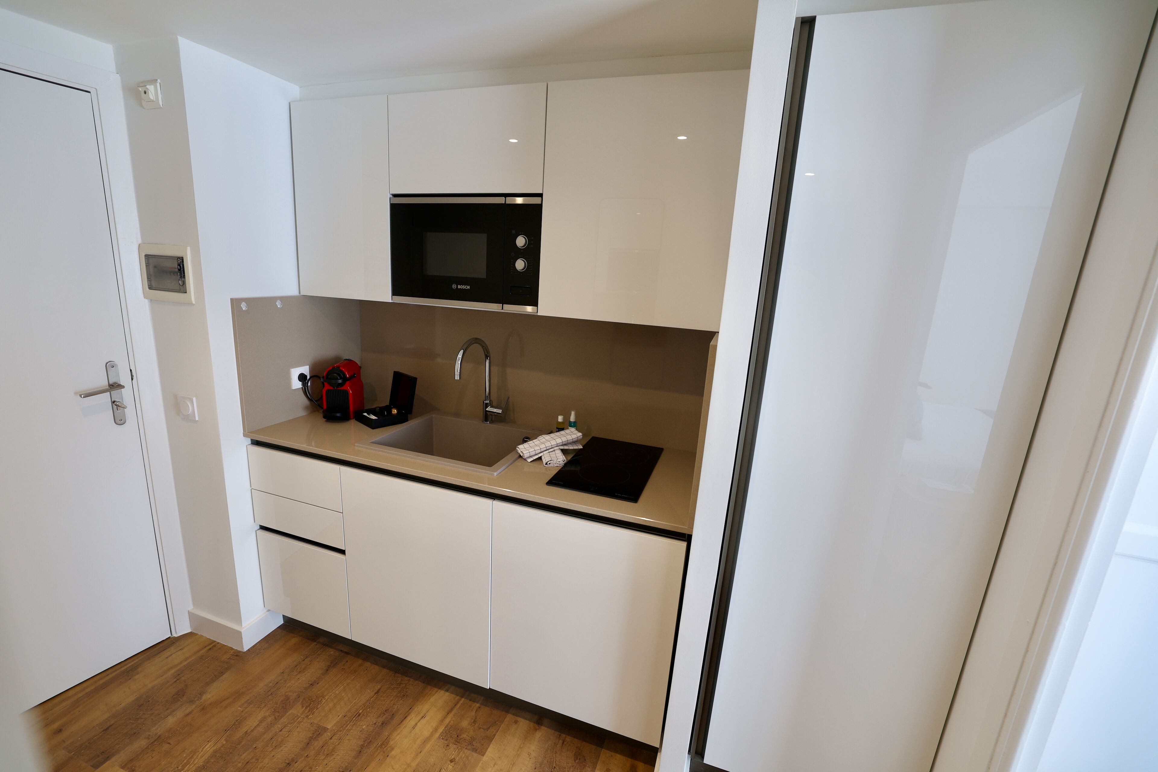 A modern kitchen with white cabinets, a black microwave, a sink, and a wooden floor.