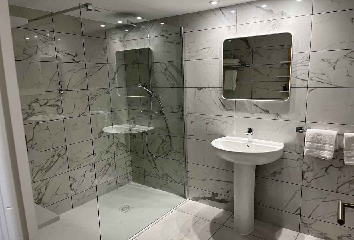 Un baño moderno con ducha envuelta en vidrio, lavamanos pedestal y un espejo grande.