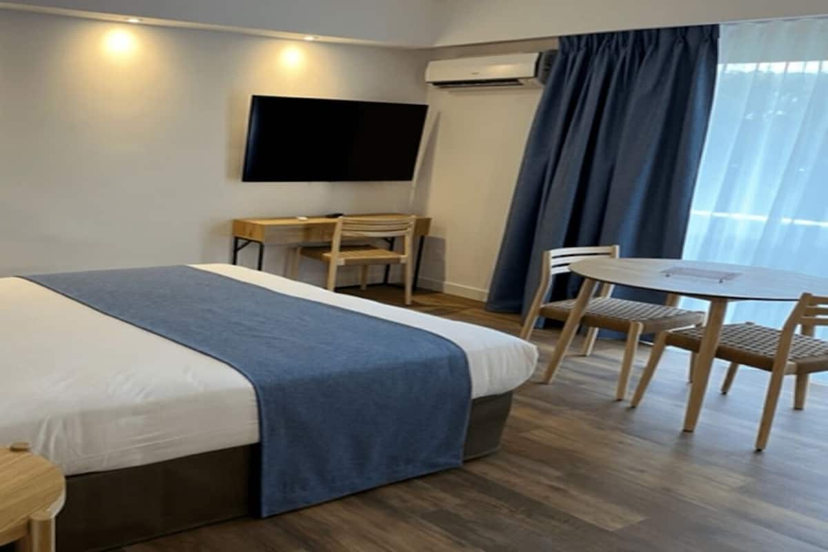 Quarto de hotel com cama, escrivaninha, cadeira, televisão e ar condicionado.