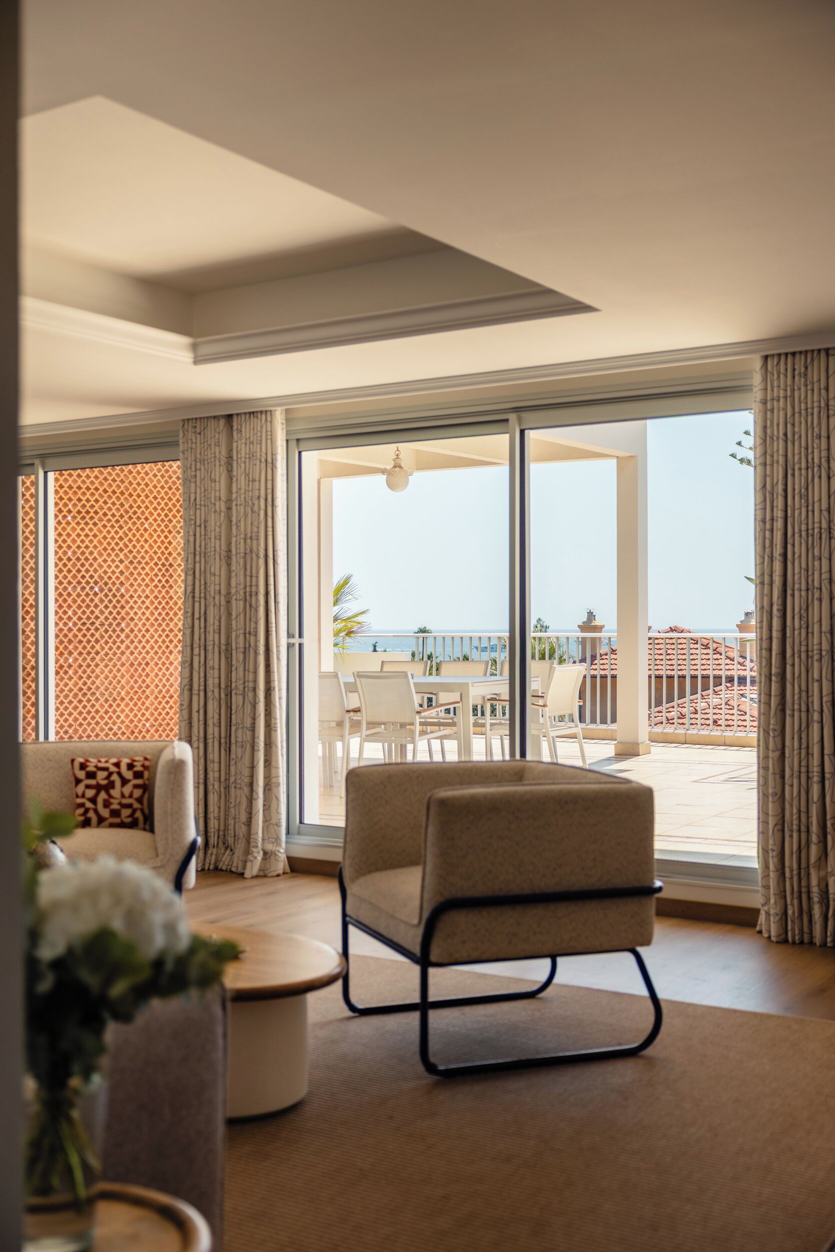 A modern living room with a large sliding glass door leading to a balcony with a view of the sea.