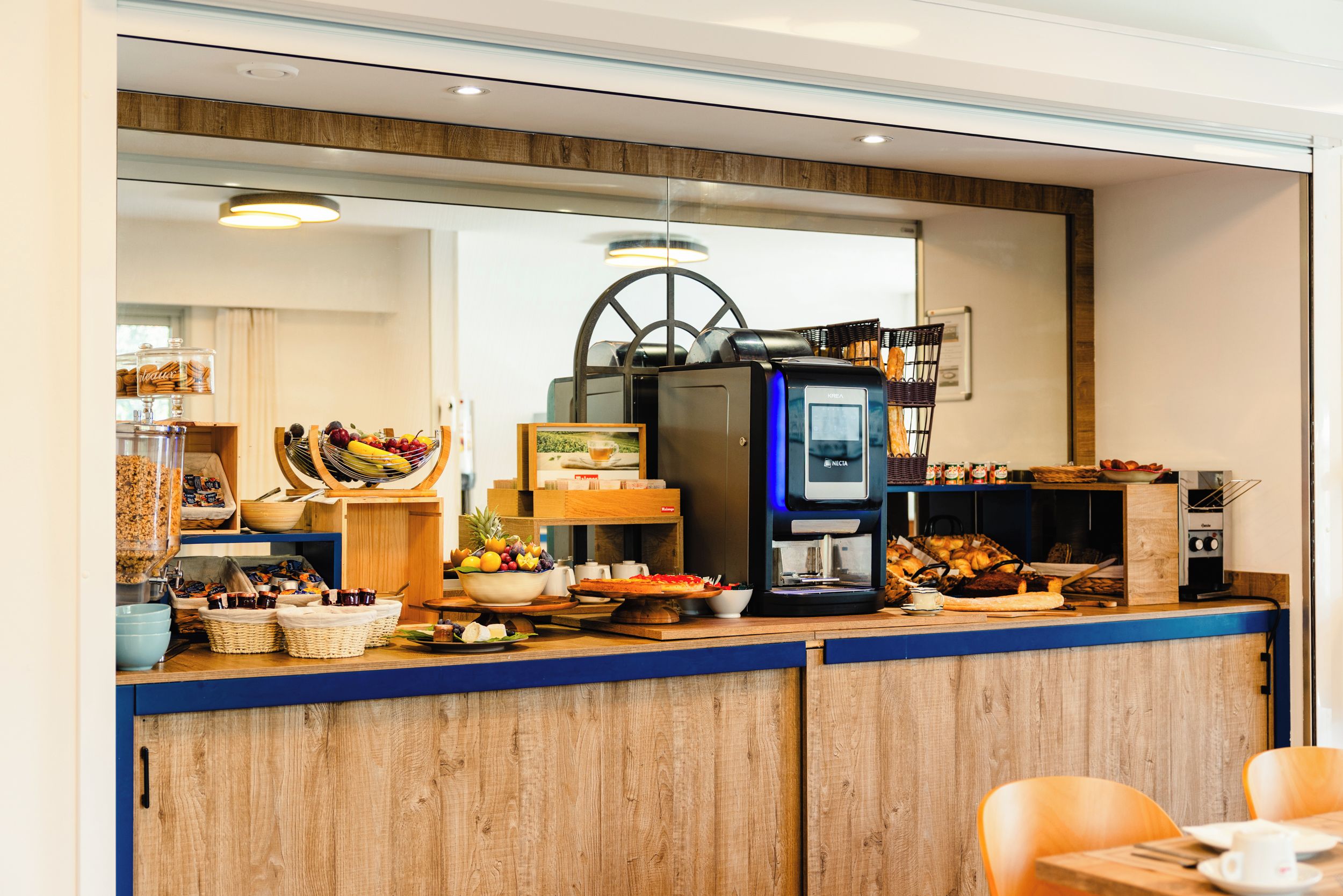 A breakfast bar with a coffee machine, fruit bowl, bread, and pastries.