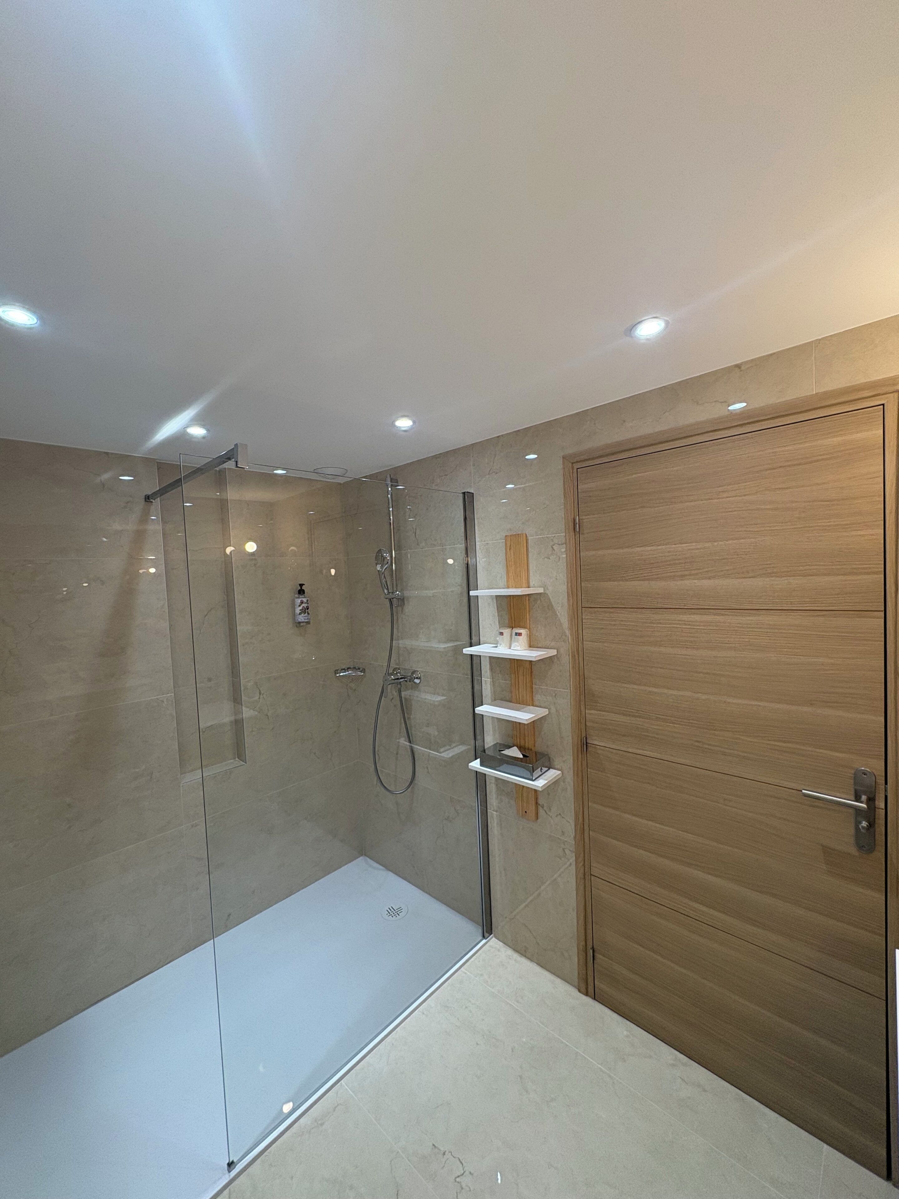 Un baño moderno con cabina de ducha de vidrio, puerta de madera y estanterías empotradas.