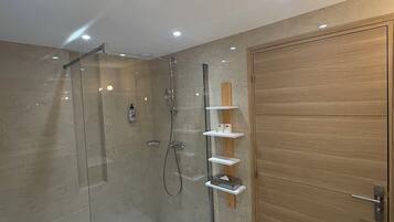 Un baño moderno con cabina de ducha de vidrio, puerta de madera y estanterías empotradas.