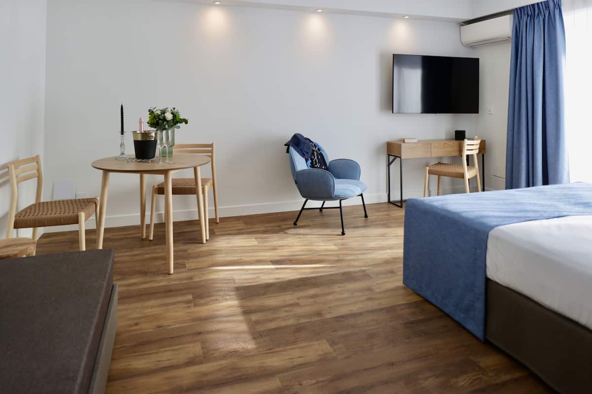 Quarto de hotel com cama, escrivaninha, cadeira, televisão e mesa de jantar com cadeiras.
