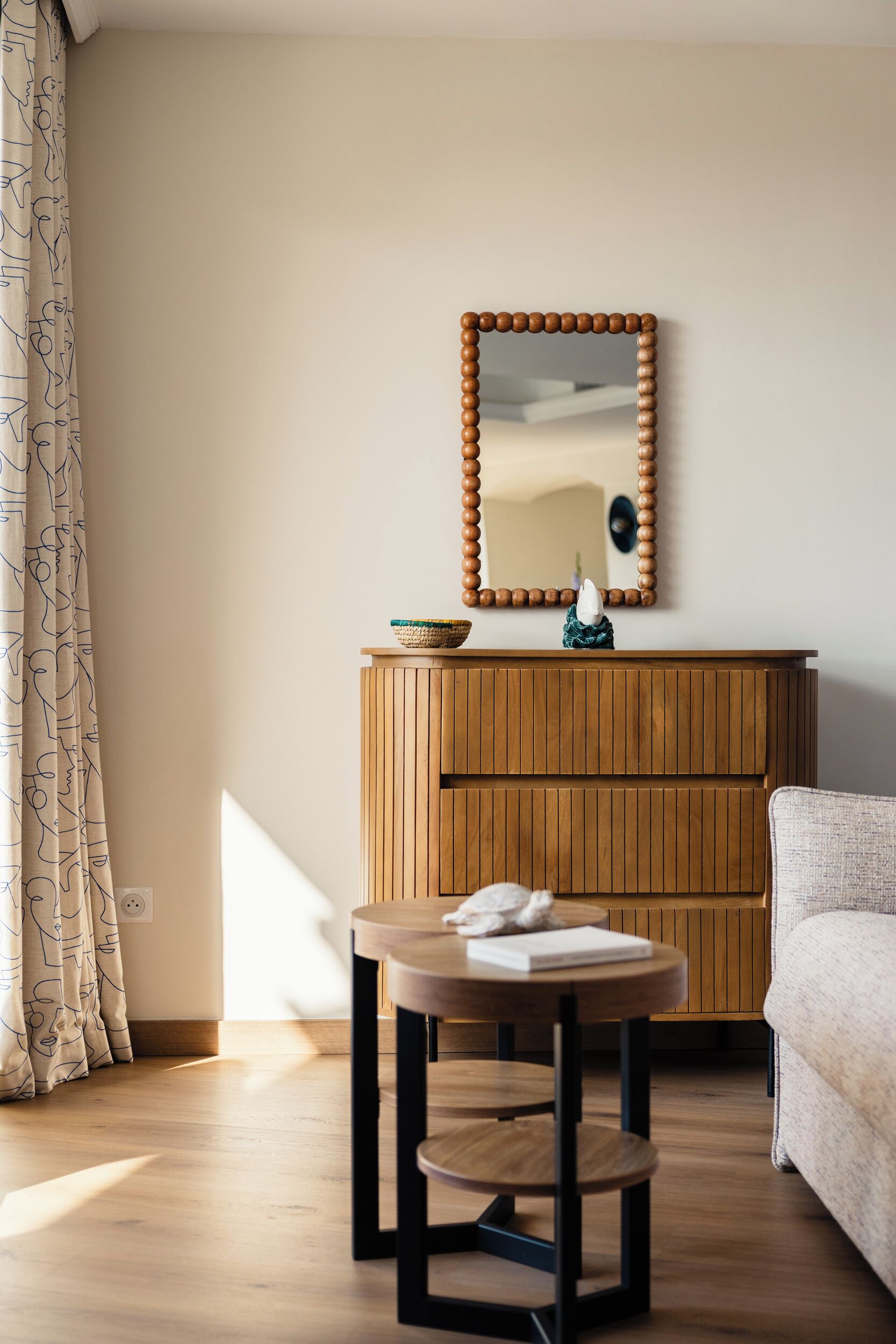 Une pièce comprenant un meuble en bois, une table ronde avec un livre, un miroir avec un cadre en bois et un canapé.