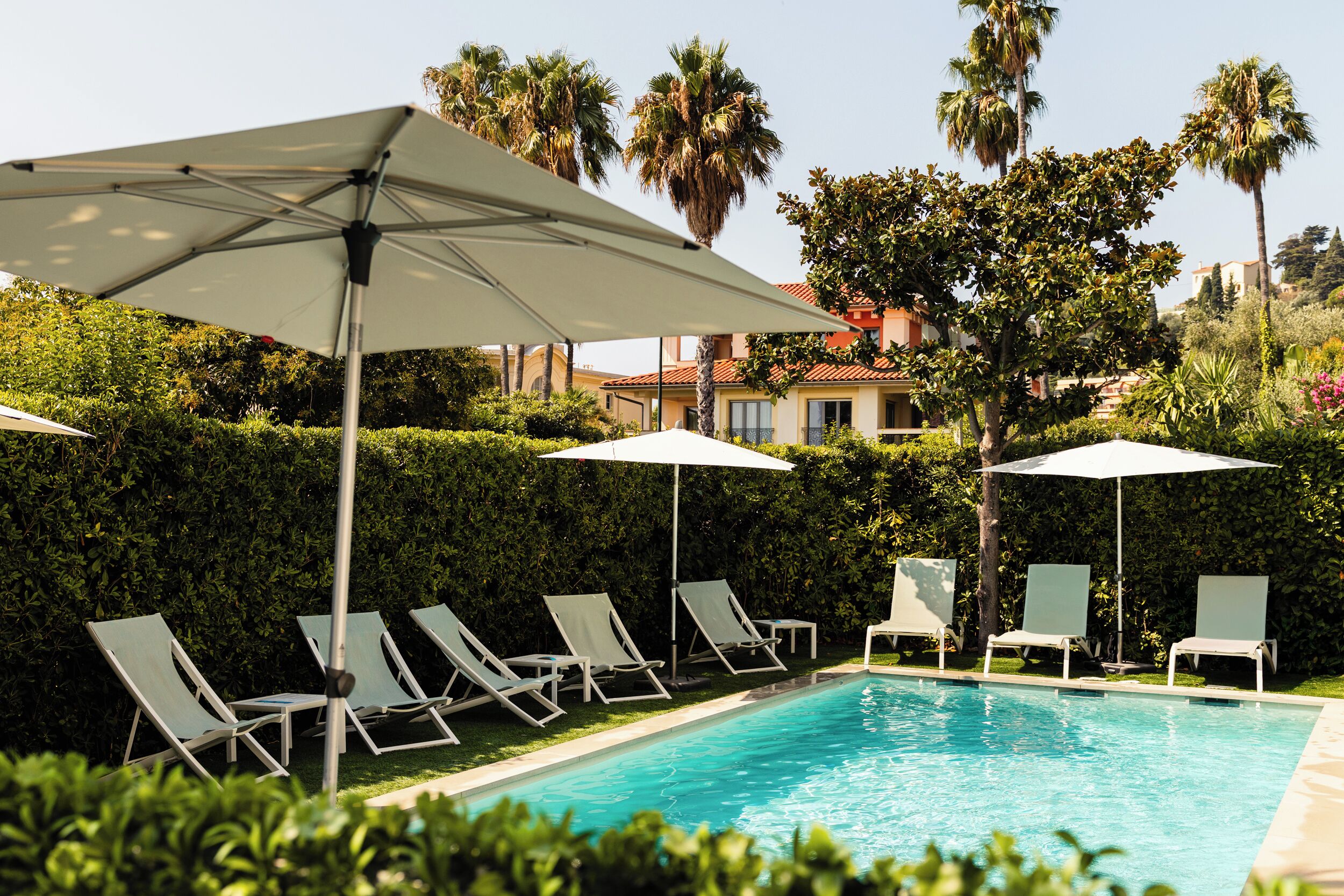 Une piscine entourée de verdure et de palmiers, avec des chaises longues et des parasols.