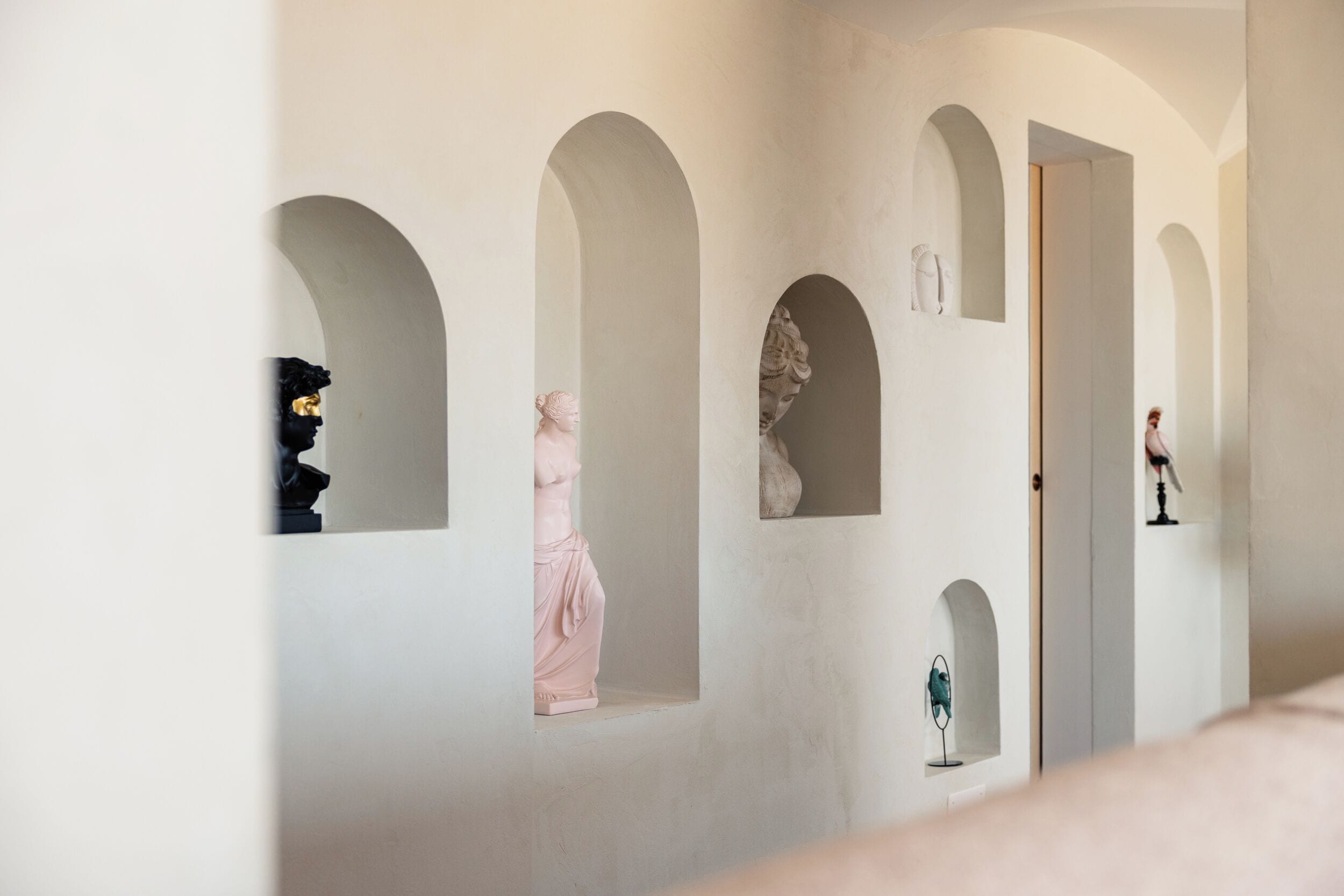 Un corridoio con porte ad arco, ognuna delle quali contiene una scultura a busto.