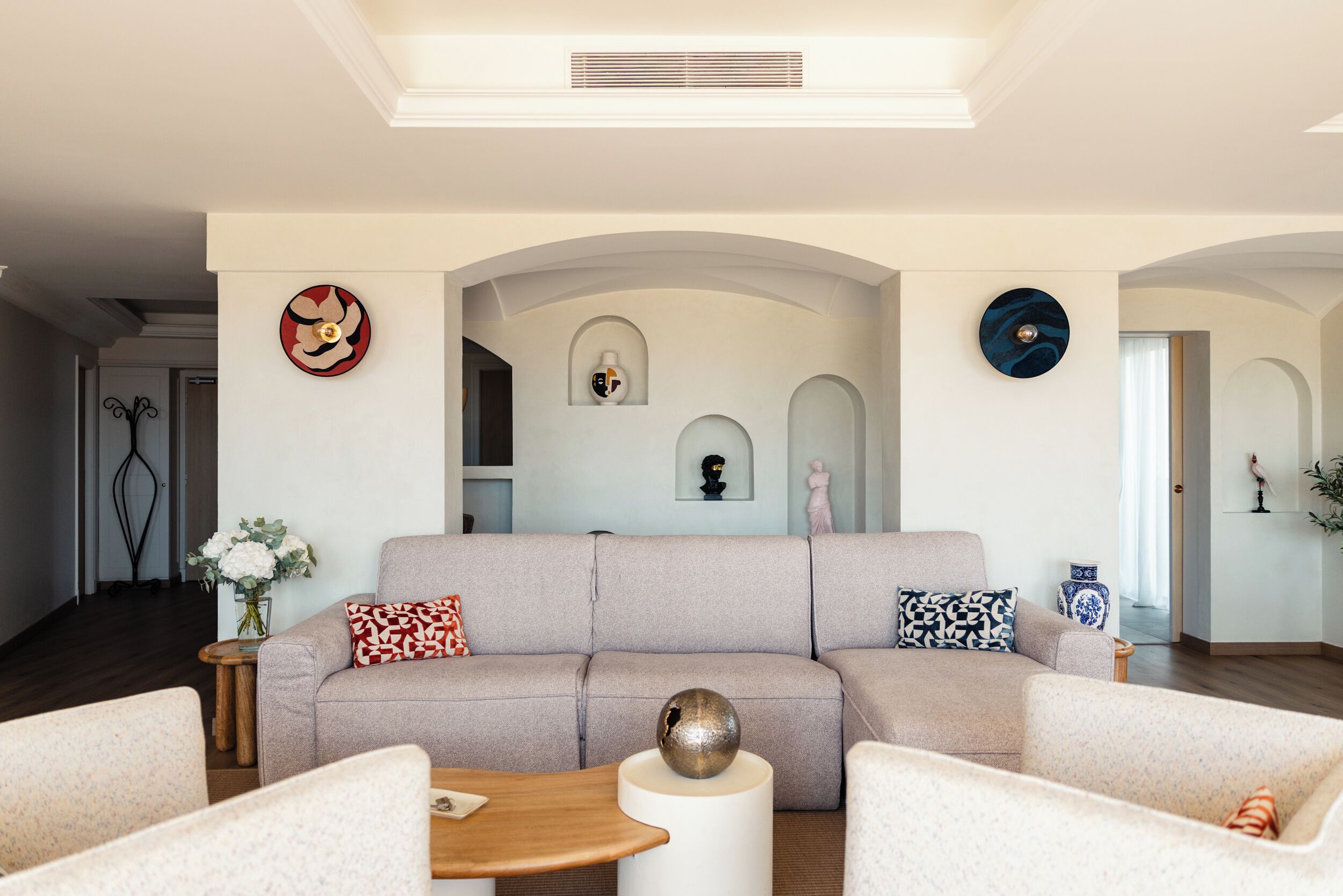 Uma sala de estar com sofá, duas poltronas, mesa de centro e objetos decorativos nas paredes.