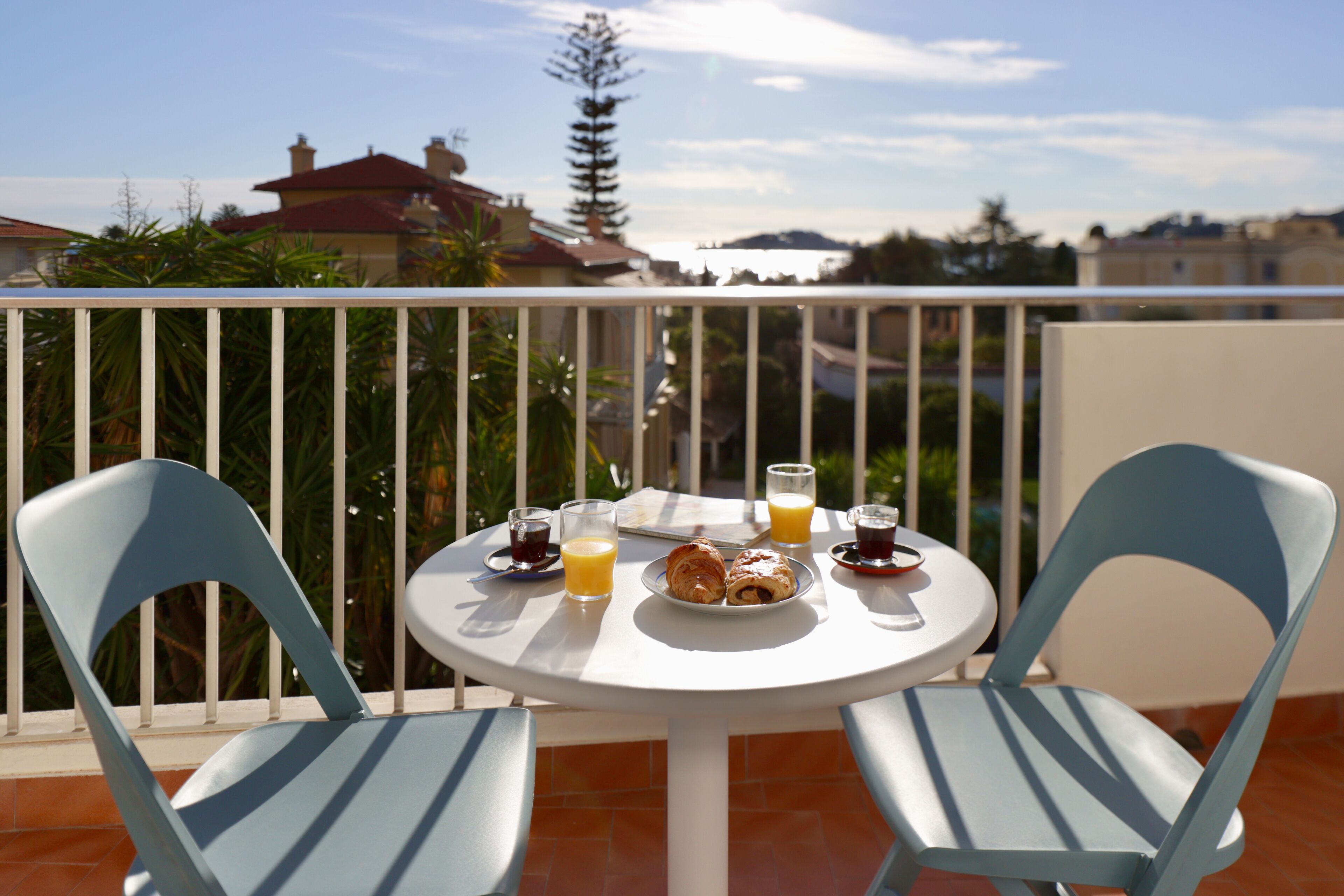 A round table with two chairs on a balcony, with a view of buildings and trees in the background.