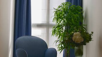 A room with a blue chair, a potted plant, and a vase on a small wooden stool.