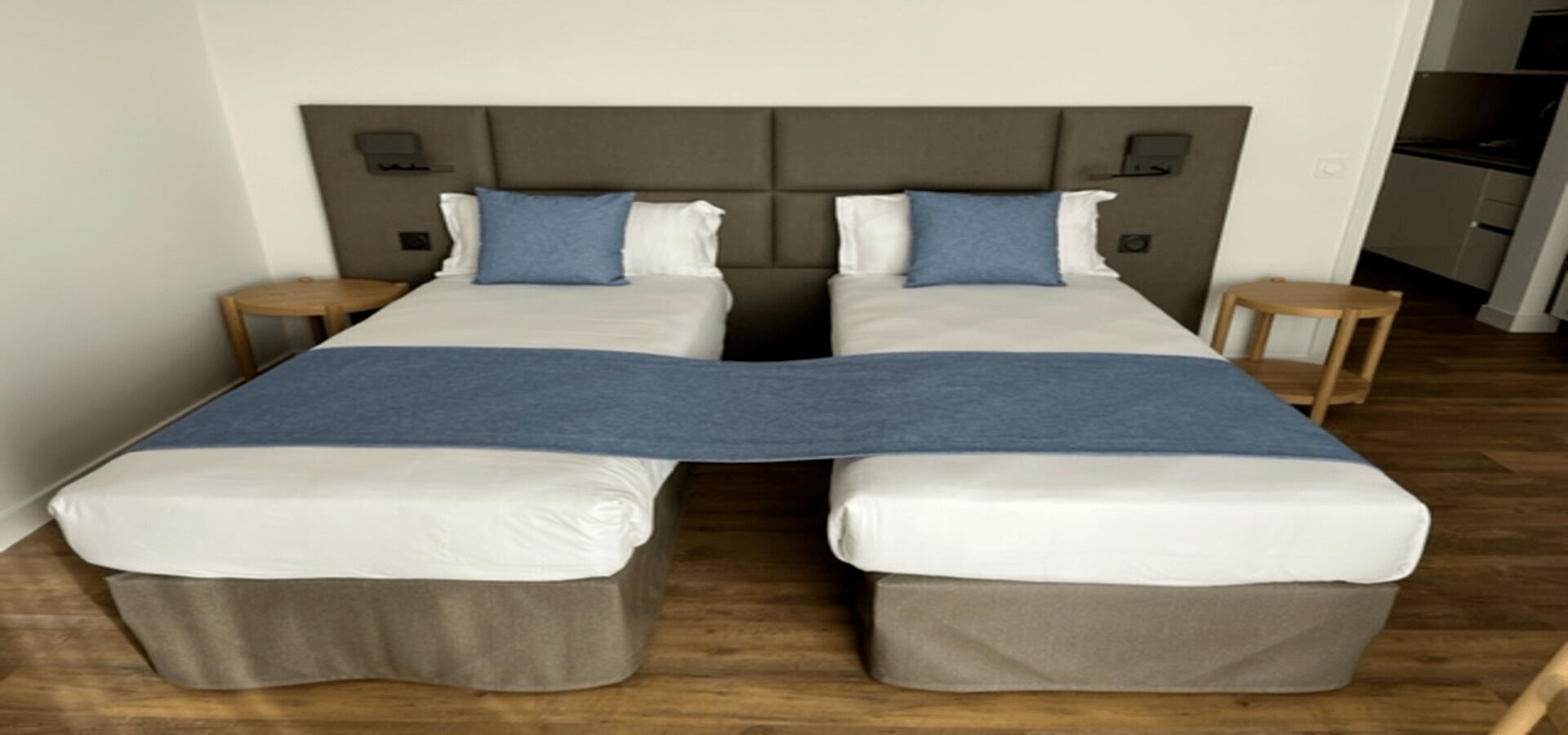 A double bed with a grey headboard, two bedside tables, and a blue throw blanket.