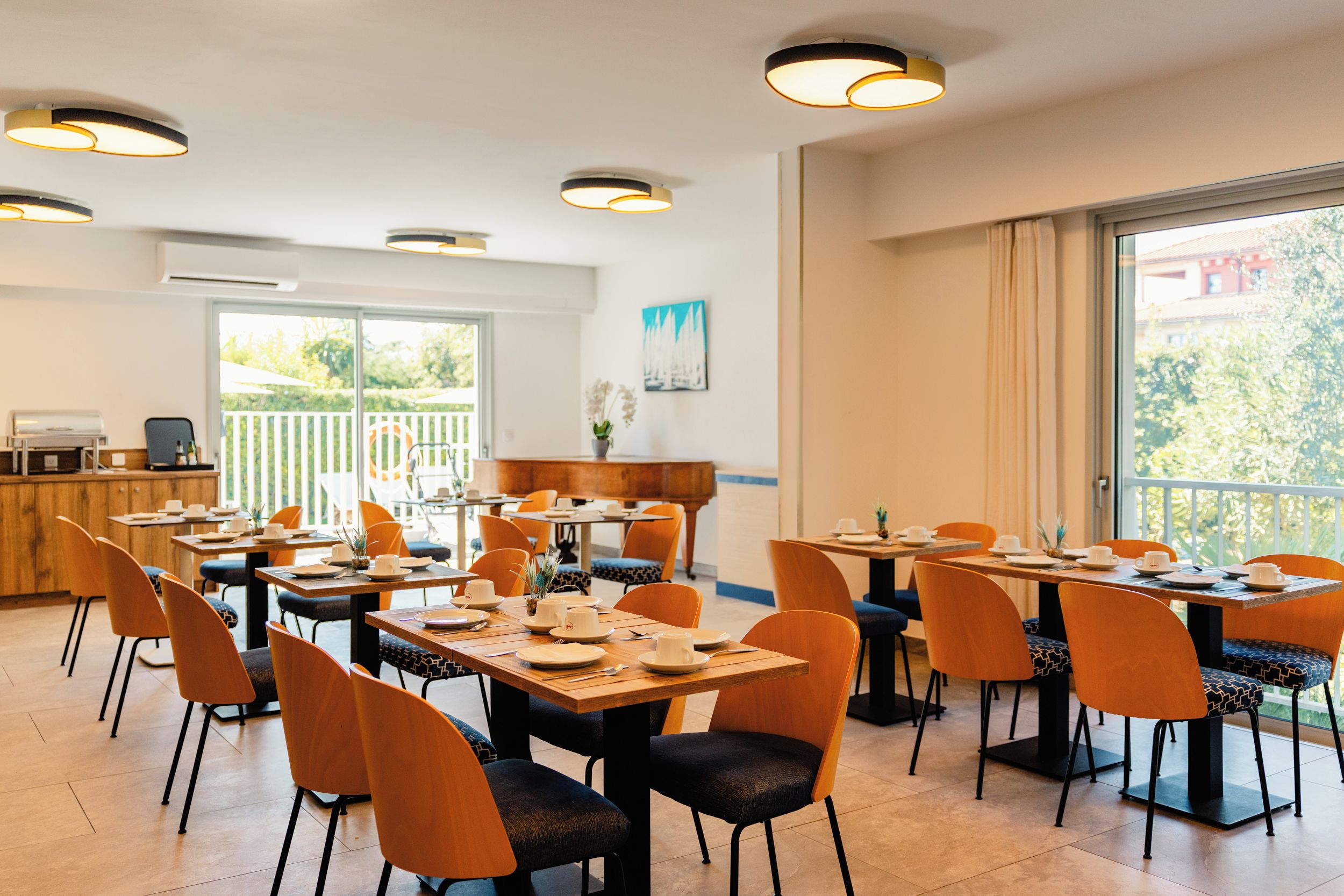 A dining area with multiple tables and chairs, a piano, and a view of greenery outside.