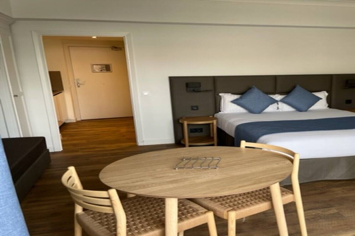 Quarto de hotel com cama, mesa de cabeceira, cadeira e uma mesa redonda.