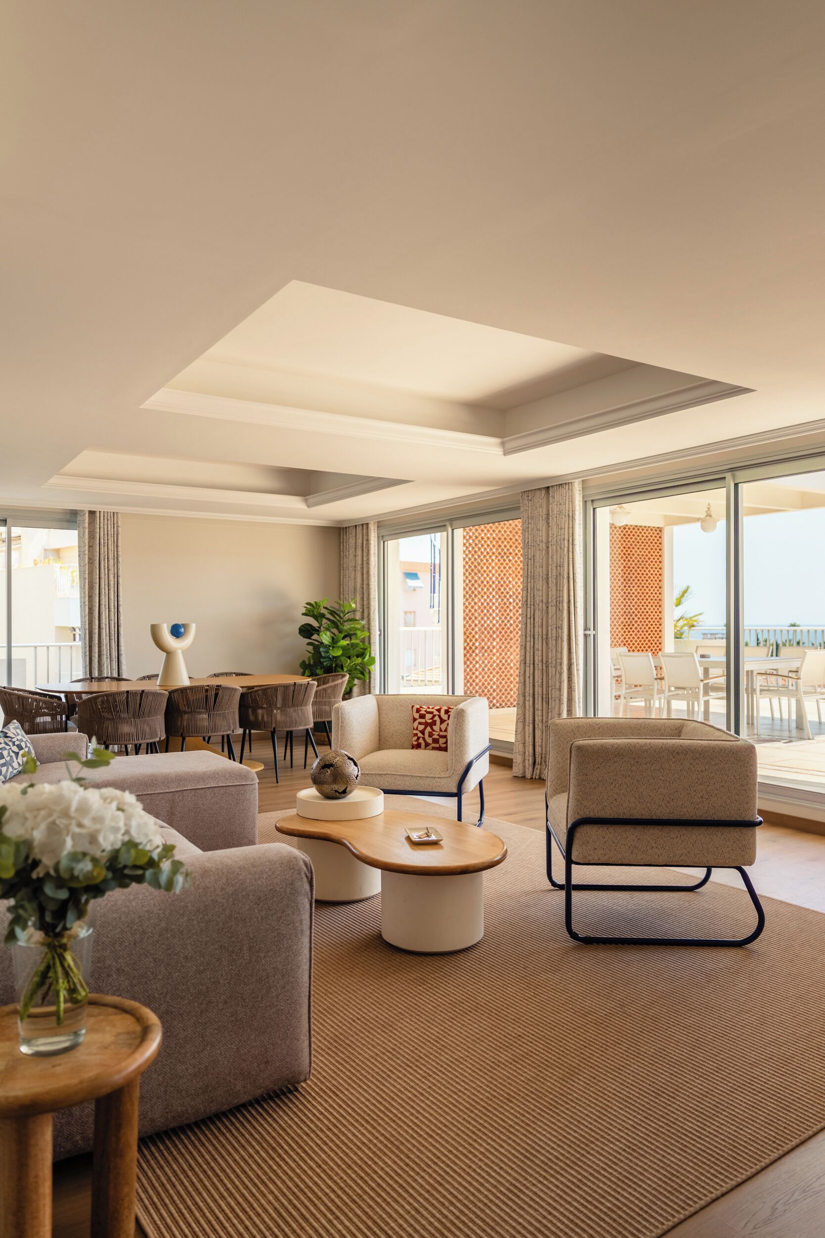 A modern living room with a sofa, armchair, coffee table, and a dining area with chairs and a table.
