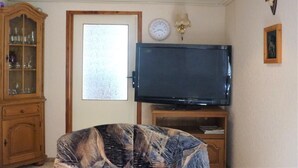 A room with a television on a stand, a wooden cabinet, a clock, and a framed picture on the wall. - Vacation home with covered terrace No pets  (Friedrichroda)