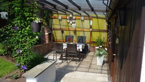 An outdoor patio with a brick barbecue, wicker furniture, and potted plants. - Vacation home with covered terrace No pets  (Friedrichroda)