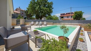 A swimming pool with lounge chairs and a table, surrounded by potted plants and a stone wall. - Villa Clariss (Visnjan)