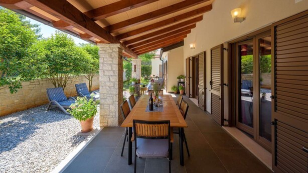 An outdoor patio with a wooden table and chairs, surrounded by stone pillars and potted plants. - Villa Clariss (Visnjan)