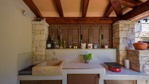 An outdoor kitchen with a stone sink, wooden cabinets, and a built-in oven. - Villa Clariss (Visnjan)